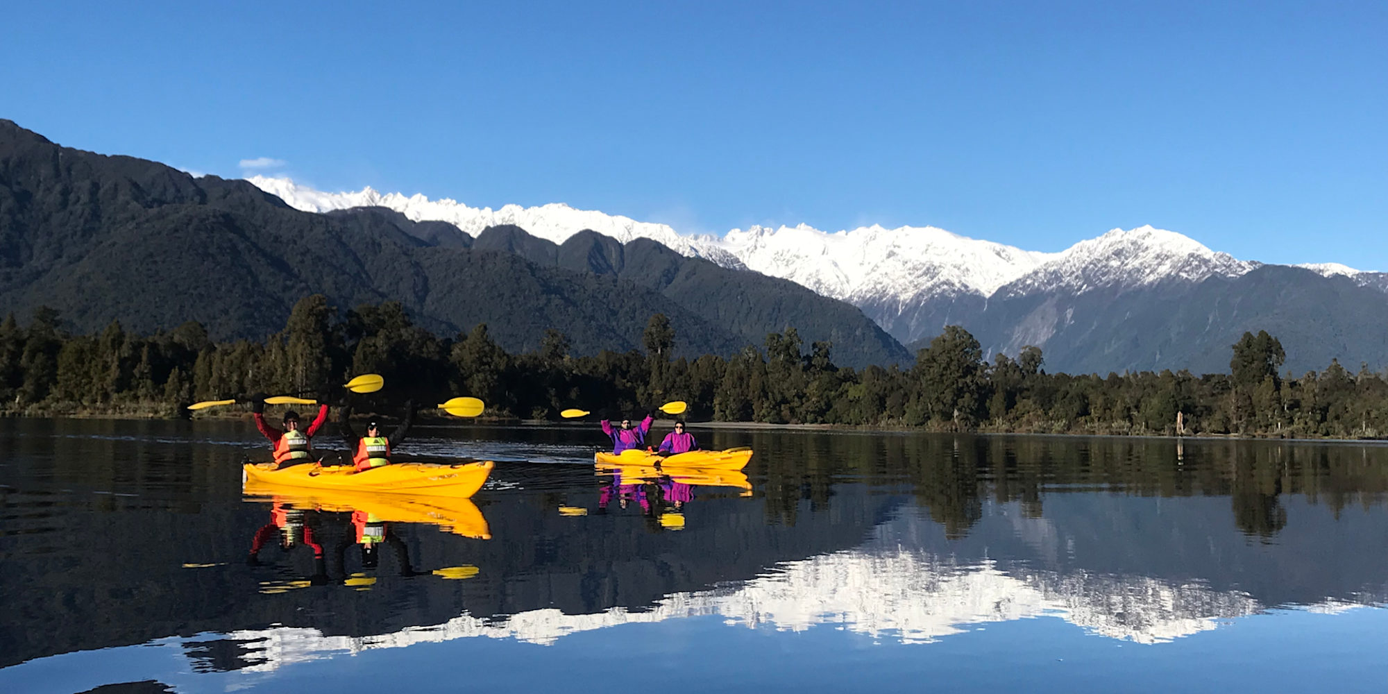 A family kayaking on New Zealand's West Coast with the Southern Alps in the background
